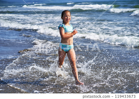 An 8 year old girl in a swimsuit having fun in the sea waves. 119433673