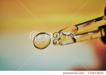 A pipette with facial serum against a sunset background in bright orange tones. A pipette with facial serum against a sunset background in bright orange tones. 119433676