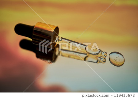 A pipette with facial serum against a sunset background in bright orange tones. A pipette with facial serum against a sunset background in bright orange tones. 119433678