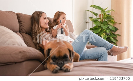 Smiling mother and girl on sofa watching TV at home Smiling mother and girl on sofa watching TV at home 119433700