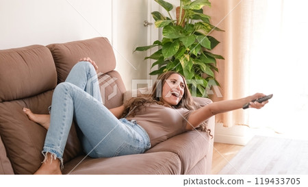 Excited woman watching TV on couch in living room at home 119433705