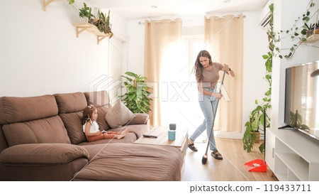 Mother sweeping floor and daughter using smartphone at home 119433711