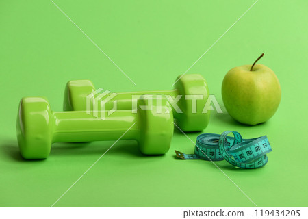 Dumbbells in bright green color, twisted measure tape and fruit 119434205