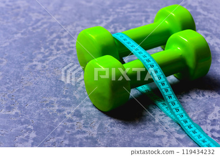 Dumbbells in green color and cyan measuring tape around them Dumbbells in green color and cyan measuring tape around them 119434232