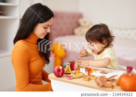 Cute little girl and mom spending good time painting autumn yellow leaves together 119434322