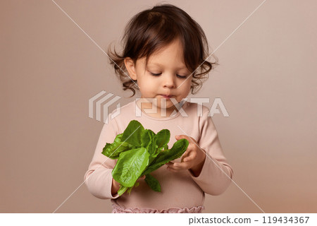 cute little child girl holding fresh green salad on beige background. healthy baby food. cute little child girl holding fresh green salad on beige background. healthy baby food. 119434367