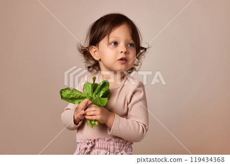 surprised child girl holding fresh green salad on beige background. healthy baby food. surprised child girl holding fresh green salad on beige background. healthy baby food. 119434368