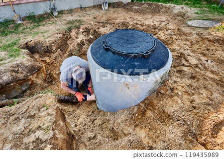 Plumber connects drainage pipe to septic tank outlet pipe to carry wastewater into drain field. 119435989