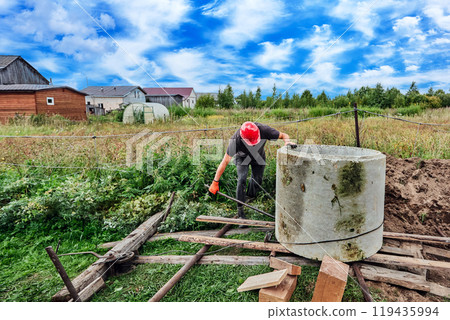 Worker moves concrete ring using roller deck made of steel pipes and boards. 119435994