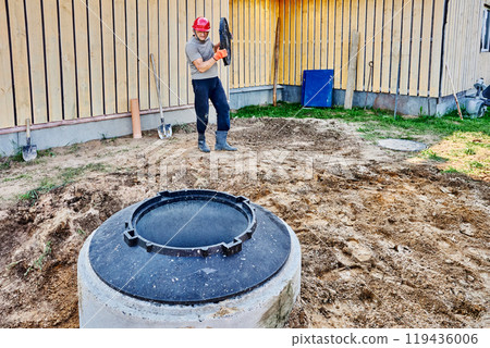 Builder carries manhole cover to cover well made of concrete rings. Builder carries manhole cover to cover well made of concrete rings. 119436006