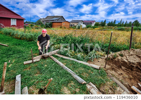 Construction worker uses manual cable winch to move load on suburban property. 119436010