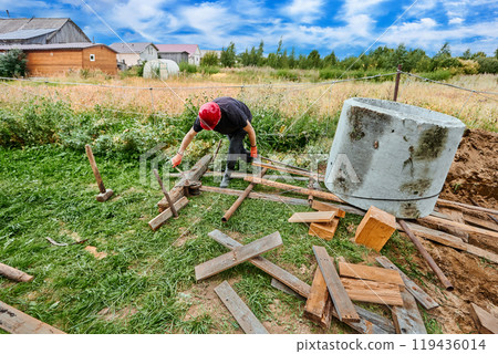 When installing next concrete ring for septic tank, builder slows its descent along roller flooring using winch. 119436014
