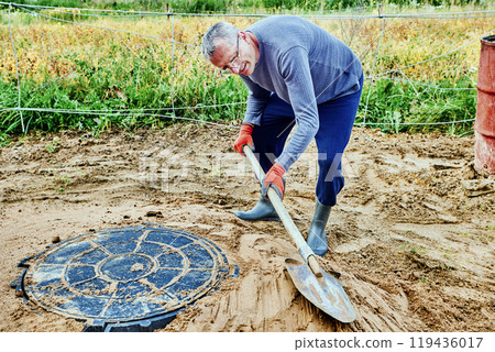 Builder poured sand around manhole cover and ramms it with shovel. 119436017