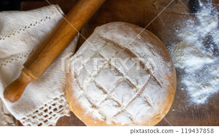 Country bread on wooden table next to a rolling pin. 119437858