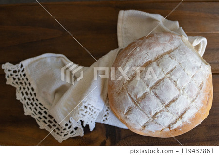 Close-up photo of a loaf of bread on a linen cloth and wooden background. Close-up photo of a loaf of bread on a linen cloth and wooden background. 119437861