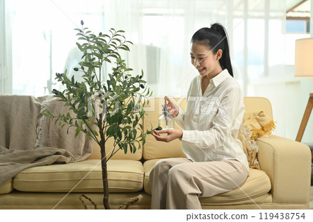 Attractive young woman taking care of plants, cleaning the leaves of houseplants at home 119438754