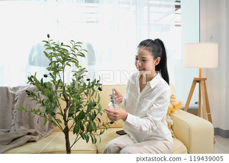 Beautiful young woman spraying water and taking care of her indoor plants 119439005