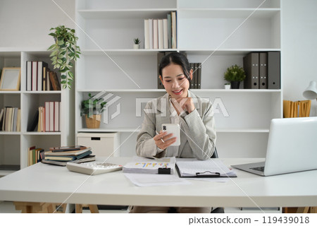 Successful young entrepreneur using smartphone at desk Successful young entrepreneur using smartphone at desk 119439018