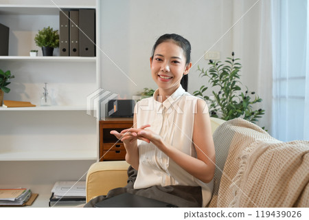 Portrait of beautiful young woman sitting on sofa and smiling at camera Portrait of beautiful young woman sitting on sofa and smiling at camera 119439026