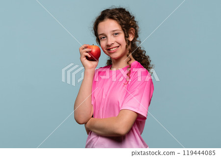 Happy girl holding red apple against cheek. Happy girl holding red apple against cheek. 119444085