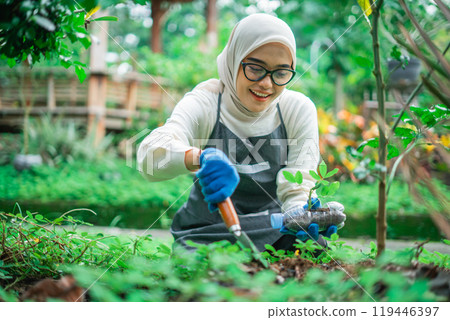 hijab woman troweling soil to plant green vegetable 119446397