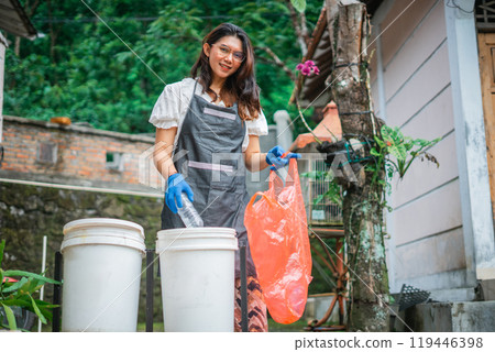 asian woman looking at camera while sorting plastic bottle into trash can 119446398