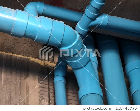 A bright blue pipes attached to a solid concrete wall 119446759