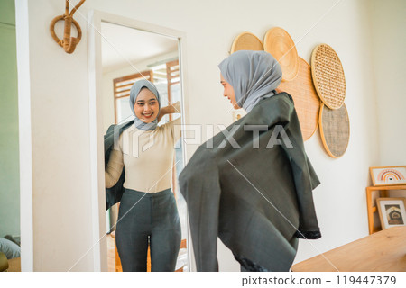 young woman wearing a blazer in front of the mirror while preparing 119447379