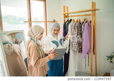 female customer in hijab chooses clothes on the shelf with a Muslim designer female customer in hijab chooses clothes on the shelf with a Muslim designer 119447397