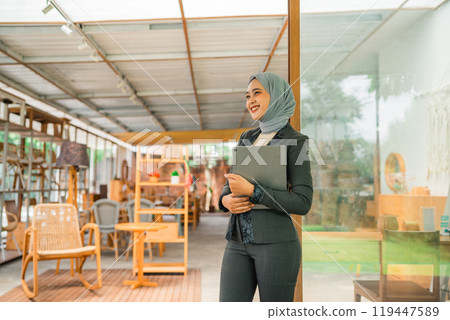 Asian Muslim woman business owner holds a tablet while working Asian Muslim woman business owner holds a tablet while working 119447589