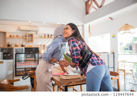 young Indonesian businesswoman kissing on both cheeks while meeting 119447644