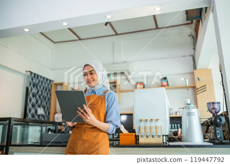 Muslim woman cafe owner using a tablet computer in a coffee cafe 119447792