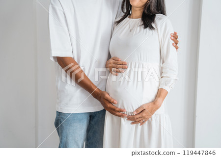 A man hugs a pregnant woman in a beautiful white dress A man hugs a pregnant woman in a beautiful white dress 119447846