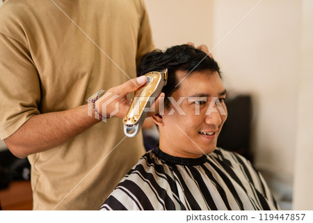 A man is currently getting his hair cut by a barber at a salon A man is currently getting his hair cut by a barber at a salon 119447857