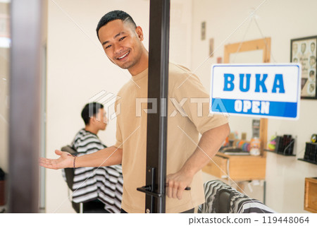 A man stands in front of a barber shop with an open sign 119448064