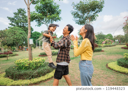 little boy lifted up by father's hand with mother while playing 119448323