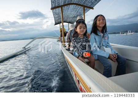 Two young girls are happily sitting together on a boat in the ocean 119448333