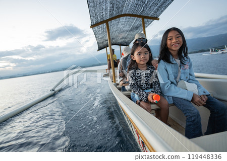 Two young girls are happily sitting on a small boat in the ocean 119448336