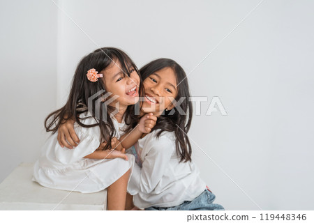 Two little girls are joyfully hugging each other while smiling brightly 119448346