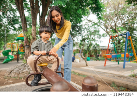 mom accompanies little boy on seesaw while playing together in the park mom accompanies little boy on seesaw while playing together in the park 119448394