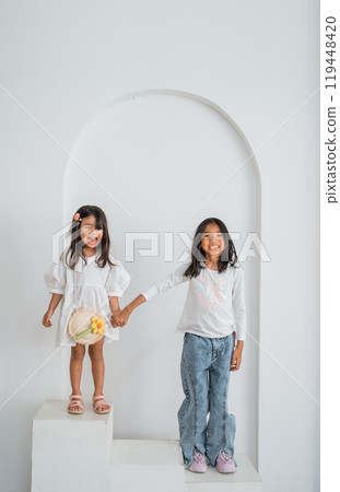 Two little girls joyfully stand together, holding hands tightly Two little girls joyfully stand together, holding hands tightly 119448420