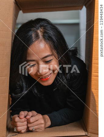 A Joyful Woman Peeking Out from a Cardboard Box in a Creative and Unique Setup 119448434