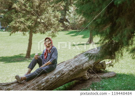 A woman, with great grace, is posing elegantly on a fallen tree located in a scenic park A woman, with great grace, is posing elegantly on a fallen tree located in a scenic park 119448484