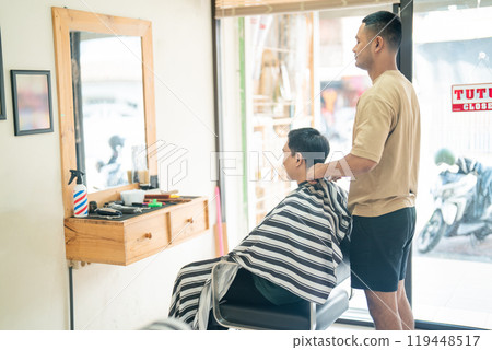 A man is currently having his hair cut at a barber shop A man is currently having his hair cut at a barber shop 119448517