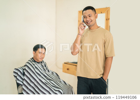 A man talks on a cell phone while another gets his hair cut 119449106