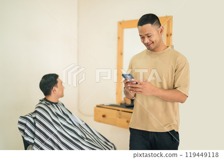 A man gets his haircut at a barber shop while another checks his phone 119449118