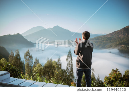 A man stands on a balcony overlooking a lake and mountains 119449220
