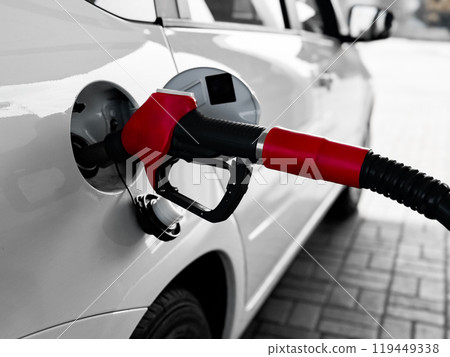 Red fuel pump refueling white car at gas station in urban setting Red fuel pump refueling white car at gas station in urban setting 119449338