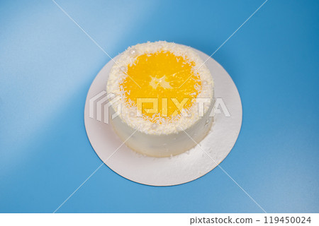 Small coconut cake decorated with an orange slice and white pearls on blue background Small coconut cake decorated with an orange slice and white pearls on blue background 119450024