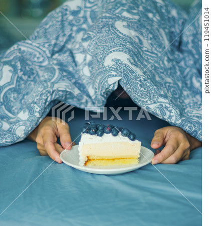 Young woman reaching hand for tasty peace of cake while lying in bed. High quality photo Young woman reaching hand for tasty peace of cake while lying in bed. High quality photo 119451014